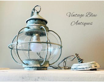 May include: Vintage blue antique lantern with a clear glass globe and metal cage. The lantern has a distressed, weathered finish and a chain for hanging. The text "Vintage Blue Antiques" is visible.