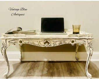 May include: A white distressed coffee table with ornate carvings and a laptop computer on top. The table has a glass top and is sitting on a wooden floor. The text "Vintage Blue Antiques" is visible in the top left corner of the image.
