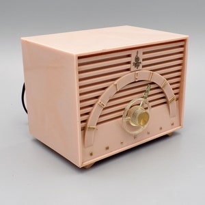 K&ouml;nnte beinhalten: Ein vintage-Radio von Emerson in rosa mit einem Drehknopf und einem "Emerson"-Label auf der Vorderseite. Das Radio hat ein Holzmaserungsmuster und ein "Duotone"-Logo mit einem Violinschl&uuml;ssel.