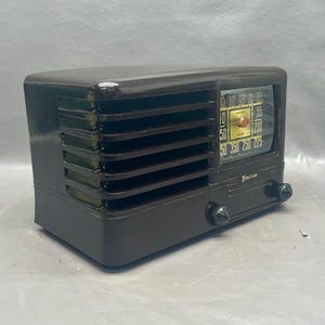 K&ouml;nnte beinhalten: Ein Vintage-Radio der Marke Zenith mit einem schwarzen Kunststoffgeh&auml;use und einem goldenen Zifferblatt. Das Radio hat ein Lautsprechergitter an der Vorderseite und zwei Kn&ouml;pfe auf der rechten Seite.