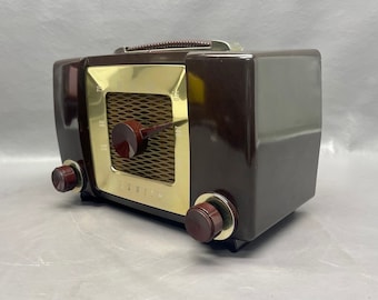 May include: A vintage Zenith radio with a brown Bakelite case and gold-colored face. The radio has a dial with numbers and a tuning knob. The radio has two knobs on the front.