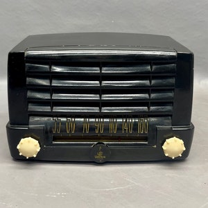 Op de afbeelding: Een zwarte vintage Zenith radio met een witte wijzerplaat en knoppen. De wijzerplaat heeft nummers van 55 tot 160.