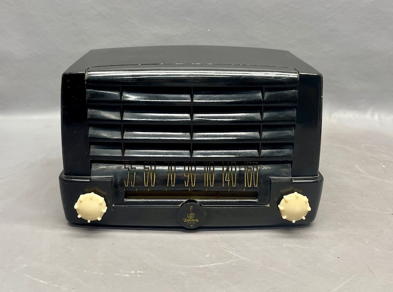Op de afbeelding: Een zwarte vintage Zenith radio met een witte wijzerplaat en knoppen. De wijzerplaat heeft nummers van 55 tot 160.