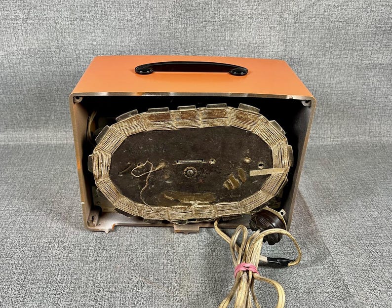 Puede incluir: Radio vintage naranja y marr&oacute;n con asa negra. Los componentes internos de la radio son visibles, incluido un gran altavoz ovalado y cableado. Se adjunta un cable de alimentaci&oacute;n con enchufe.