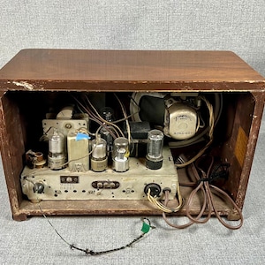 May include: Vintage wooden radio with the back removed, revealing internal components. The radio's wooden cabinet is a dark brown color. Visible components include vacuum tubes, wiring, and a speaker. The model number is visible on the front panel.