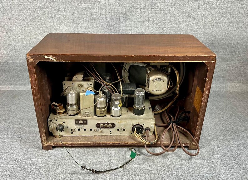 May include: Vintage wooden radio with the back removed, revealing internal components. The radio's wooden cabinet is a dark brown color. Visible components include vacuum tubes, wiring, and a speaker. The model number is visible on the front panel.