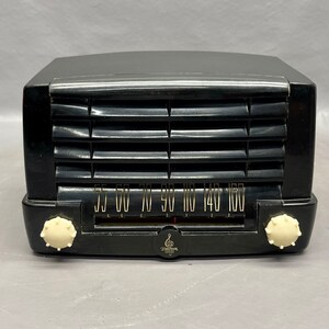 May include: A black vintage Zenith radio with a white dial and knobs. The radio has a grille on the front and a tuning dial with numbers from 55 to 160.