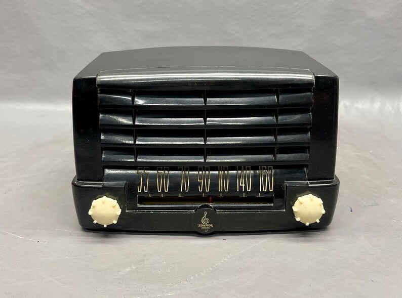 May include: A black vintage Zenith radio with a white dial and knobs. The radio has a grille on the front and a tuning dial with numbers from 55 to 160.