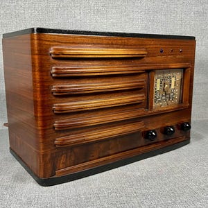 May include: A vintage wooden radio with a dark finish. The radio features horizontal slats across the front, a square dial, and three black knobs. The top and base are black, and the overall design is rectangular.