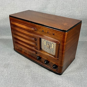 May include: A vintage wooden radio with a dark brown finish. The radio has a rectangular shape with a speaker grill on the front and a dial display. It features black knobs and a glossy top.