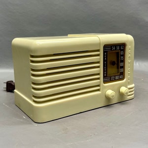 May include: A vintage off-white RCA Victor table radio with a brown dial and knobs. The dial has numbers from 54 to 145.
