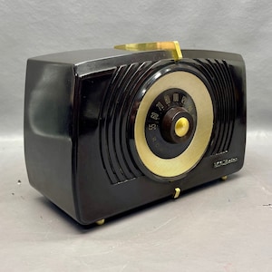 May include: A vintage black Bakelite radio with a gold dial and tuning knob. The radio has a rounded rectangular shape and a sleek design.