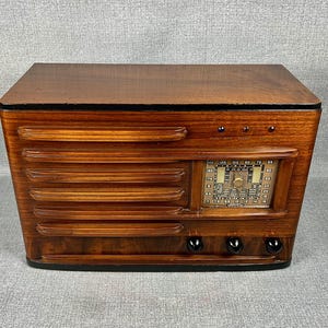 May include: A vintage wooden radio with a dark brown finish. The radio features a speaker grill design on the front, a tuning dial, and several knobs. The radio's design is reminiscent of mid-century modern aesthetics.