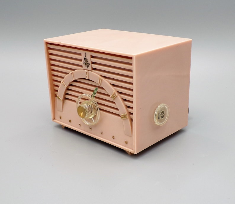 K&ouml;nnte beinhalten: Ein vintage-Radio von Emerson in rosa mit einem goldenen Zifferblatt und einem Drehknopf. Das Radio hat ein Holzmaserungsmuster und das Wort "Emerson" ist auf der Vorderseite aufgedruckt.