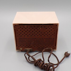 K&ouml;nnte beinhalten: Ein rosafarbenes Vintage-Radio von Emerson mit einem braunen Lautsprechergitter und einem Warnhinweis mit dem Text: "THIS COVER IS EQUIPPED WITH AN INTERLOCK TO PREVENT DANGEROUS ELECTRICAL SHOCK FOR SERVICING, REMOVE SCREWS PULL COVER COMPLETELY OUT Op от ZAMPER TH INTERLOCK PLUG OR ITS SAFE OF FEATURE WILL BE DESTROYED EMIRSON RADIO PHONOGRAPH  MADE IN U.S.A."