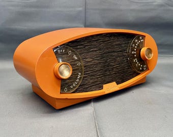 May include: An orange vintage radio with a woodgrain speaker and a clear plastic dial with volume and on/off controls.