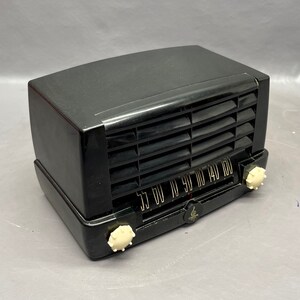 May include: A black vintage radio with a white dial and knobs. The radio has a metal grille and a black plastic case.