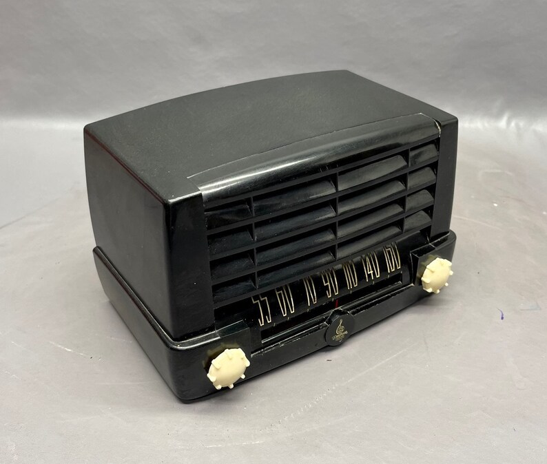 May include: A black vintage radio with a white dial and knobs. The radio has a metal grille and a black plastic case.