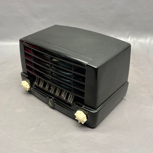 May include: A black vintage radio with a white dial and knobs. The radio has a grill on the front and a black plastic case.