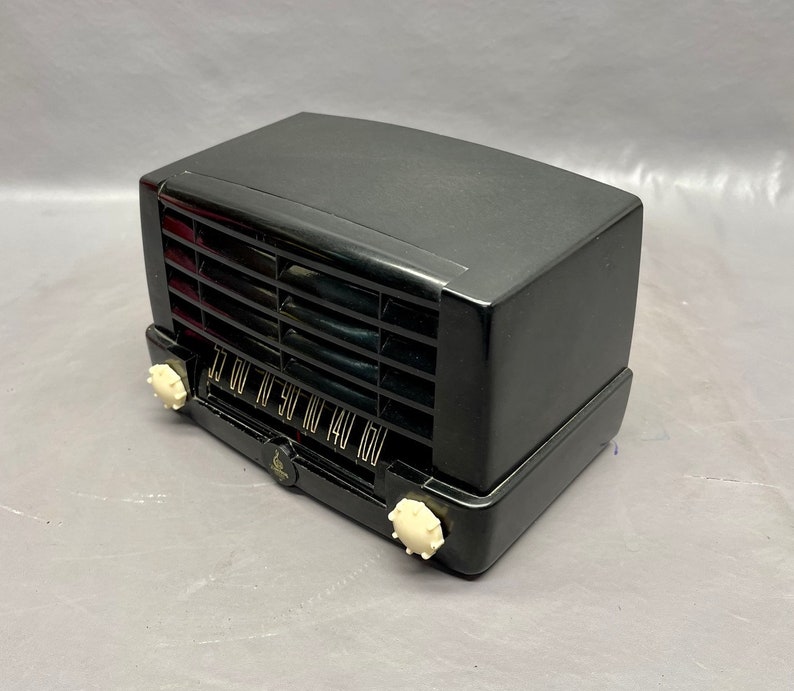 May include: A black vintage radio with a white dial and knobs. The radio has a grill on the front and a black plastic case.