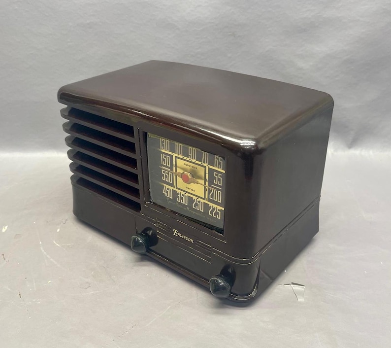 K&ouml;nnte beinhalten: Ein braunes Vintage-Radio von Emerson mit einem Zifferblatt, das von 130 bis 65, von 150 bis 55, von 550 bis 200, von 450 bis 225, von 350 bis 250 reicht. Das Radio hat zwei Kn&ouml;pfe an der Vorderseite.