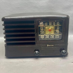 K&ouml;nnte beinhalten: Ein braunes Vintage-Radio von Emerson mit einem schwarzen Zifferblatt und einer goldfarbenen Tuningskala. Das Radio hat ein Lautsprechergitter an der Vorderseite und einen Knopf an jeder Seite.