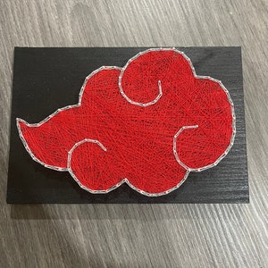 May include: A red cloud design made of string art on a black rectangular wooden board. The cloud is outlined in white and filled with red string. The artwork is displayed on a gray wooden surface.