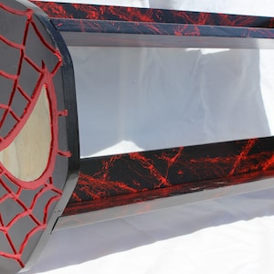 May include: A black and red wooden shelf with a carved Spider-Man design on the side. The shelf has a red and black marbled finish.