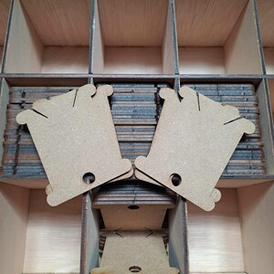 Op de afbeelding: Twee bruine houten draadhaspels met een gat in het midden. De haspels zijn op elkaar gestapeld en bevinden zich in een houten doos.