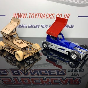 May include: Two toy stock car models. One is made of wood and is unpainted. The other is painted blue with a red wing. Both models have a similar design with a raised wing and four wheels.