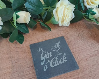 May include: A black slate coaster with the text "it's Gin o'Clock" in white lettering. A small illustration of a cocktail glass with a garnish is above the text.