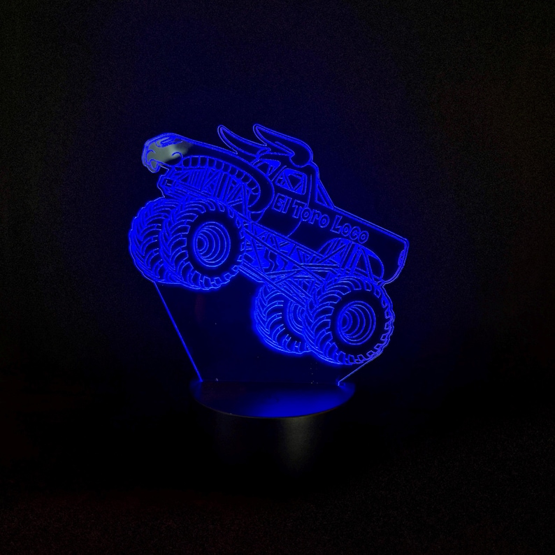 May include: A blue LED night light shaped like a monster truck with the text "El Toro Loco". The truck has large tires and a bull head design. The light is on a black base and emits a bright blue glow.