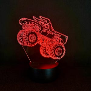 May include: A red LED night light shaped like a monster truck with the text "El Toro Loco". The truck has large tires and a detailed design. The light sits on a black base and emits a red glow.