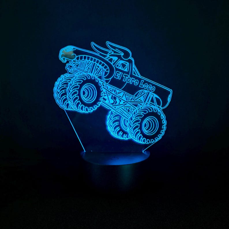 May include: A blue LED night light featuring a monster truck design with the text "El Toro Loco." The truck has large tires and a bull head emblem. The light is on a black base and emits a bright blue glow.