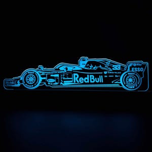May include: A blue silhouette of a Formula 1 racing car with the words "Red Bull" and "Aston Martin" on the side. The car has sponsor logos including "Mobil 1", "TAG Heuer", "Esso", and "AT&T".