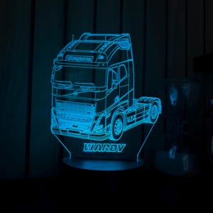 May include: A blue LED night light shaped like a semi-truck. The truck's outline is illuminated, with the name "WARDY" displayed at the base. The light is on a dark surface.