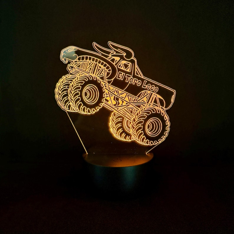 May include: A glowing LED night light featuring a monster truck design. The truck is outlined in a warm yellow light, with the words "El Toro Loco" visible on the side. The light sits on a small, round base.