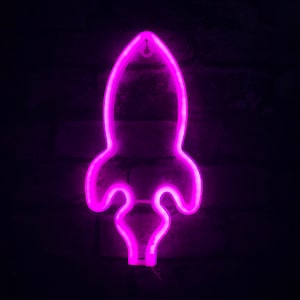 Könnte beinhalten: Ein pinkfarbenes Neonlicht in Form einer Rakete. Das Licht befindet sich an einer dunklen Backsteinwand.