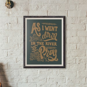 May include: A framed print with a dark green background and gold lettering. The text reads "As I went down in the river to pray".