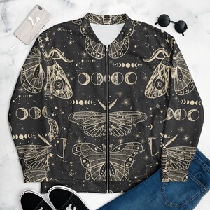 Può includere: Giacca bomber nera con un design celeste di falene e fasi lunari. La giacca presenta una cerniera completa e un interno bianco. Le falene e le lune sono di colore crema, su uno sfondo nero con stelle.