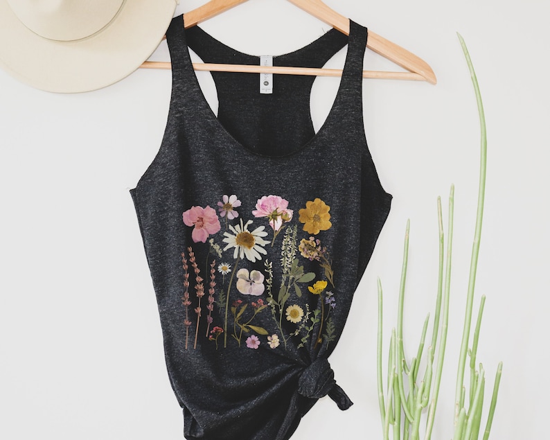 May include: A black tank top with a floral print featuring pressed flowers in shades of pink, yellow, and white. The tank top is made of a soft, comfortable material and has a racerback style.