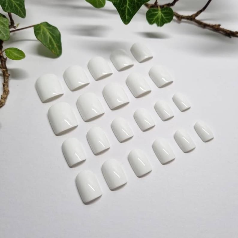 May include: A set of 24 white oval-shaped false nails arranged in rows on a white surface.