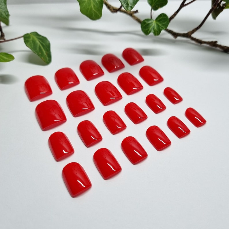 May include: A set of 20 red false nails in various sizes. The nails are arranged in rows on a white surface.