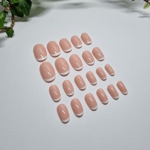 May include: A set of 20 oval-shaped false nails with a white tip design. The nails are a light pink color and are arranged in rows on a white surface.