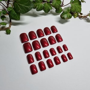 Könnte beinhalten: Ein Set mit 20 falschen Nägeln in verschiedenen Größen in Burgunderrot. Die Nägel sind in Reihen auf einer weißen Oberfläche angeordnet.