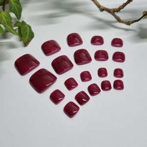 Könnte beinhalten: Ein Set mit 18 burgunderfarbenen Zehennagelspitzen in verschiedenen Größen. Die Spitzen sind fächerförmig auf einer weißen Oberfläche angeordnet.