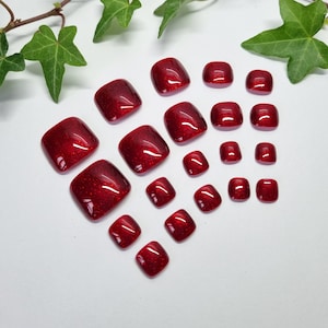 May include: A set of 20 red glitter toe nail wraps in various sizes. The wraps are square shaped and have a sparkly finish.