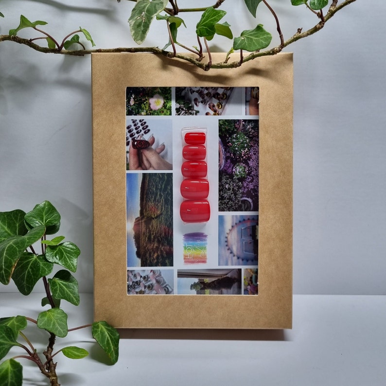 May include: A set of five red press-on nails in a clear plastic case. The nails are arranged vertically in the case.