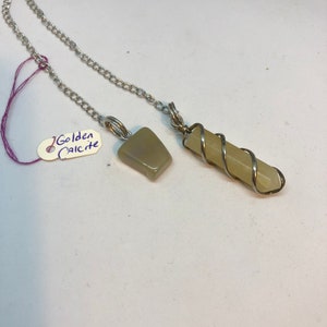 Może przedstawiać: Dwa zielone kryształowe wahadła na srebrnym łańcuszku. Wahadła mają kształt kwadratowy i długi, cienki kształt. Etykieta "Golden Calcite" jest widoczna na zdjęciu.