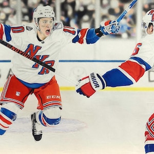 May include: Two hockey players wearing white and blue jerseys with red accents. The player on the left is holding a hockey stick and is in a skating position. The player on the right is reaching out with their left hand. Both players are wearing helmets with the letters "NYR" on them.
